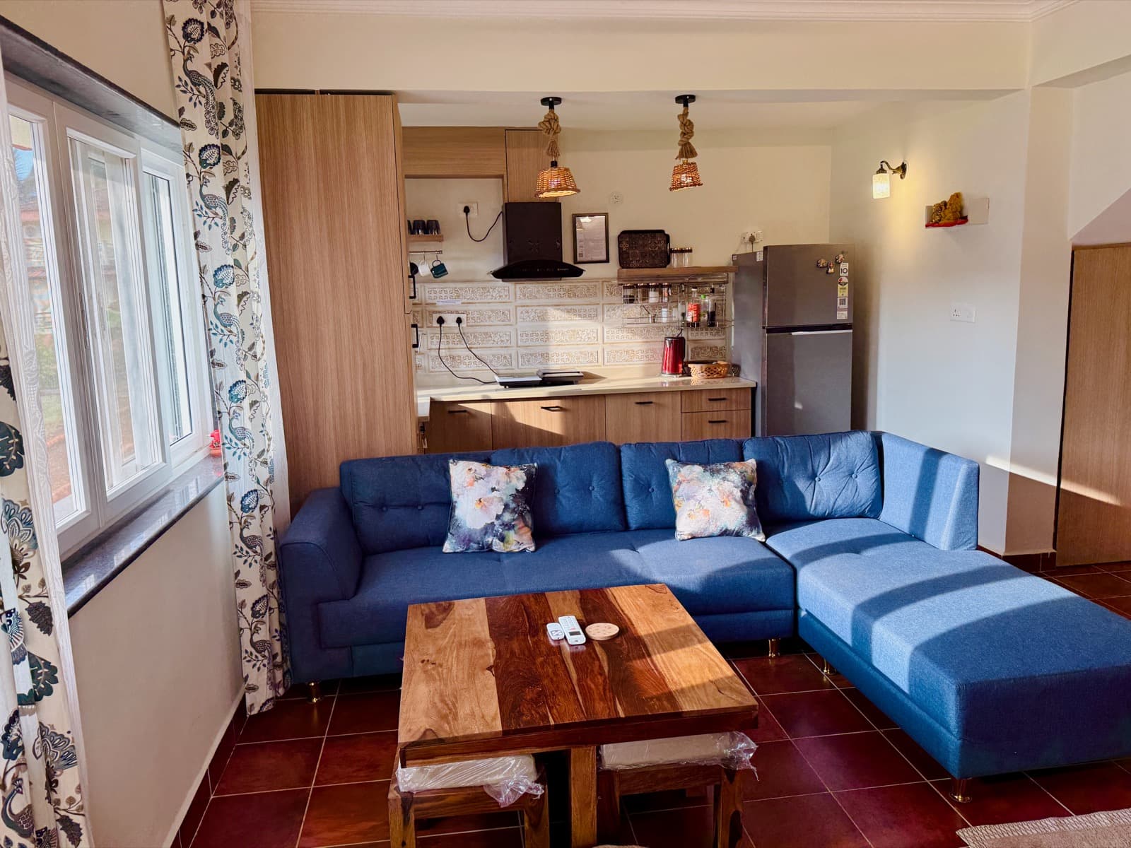 The 1 BHK's living room, blue corner sofa and open kitchen behind it