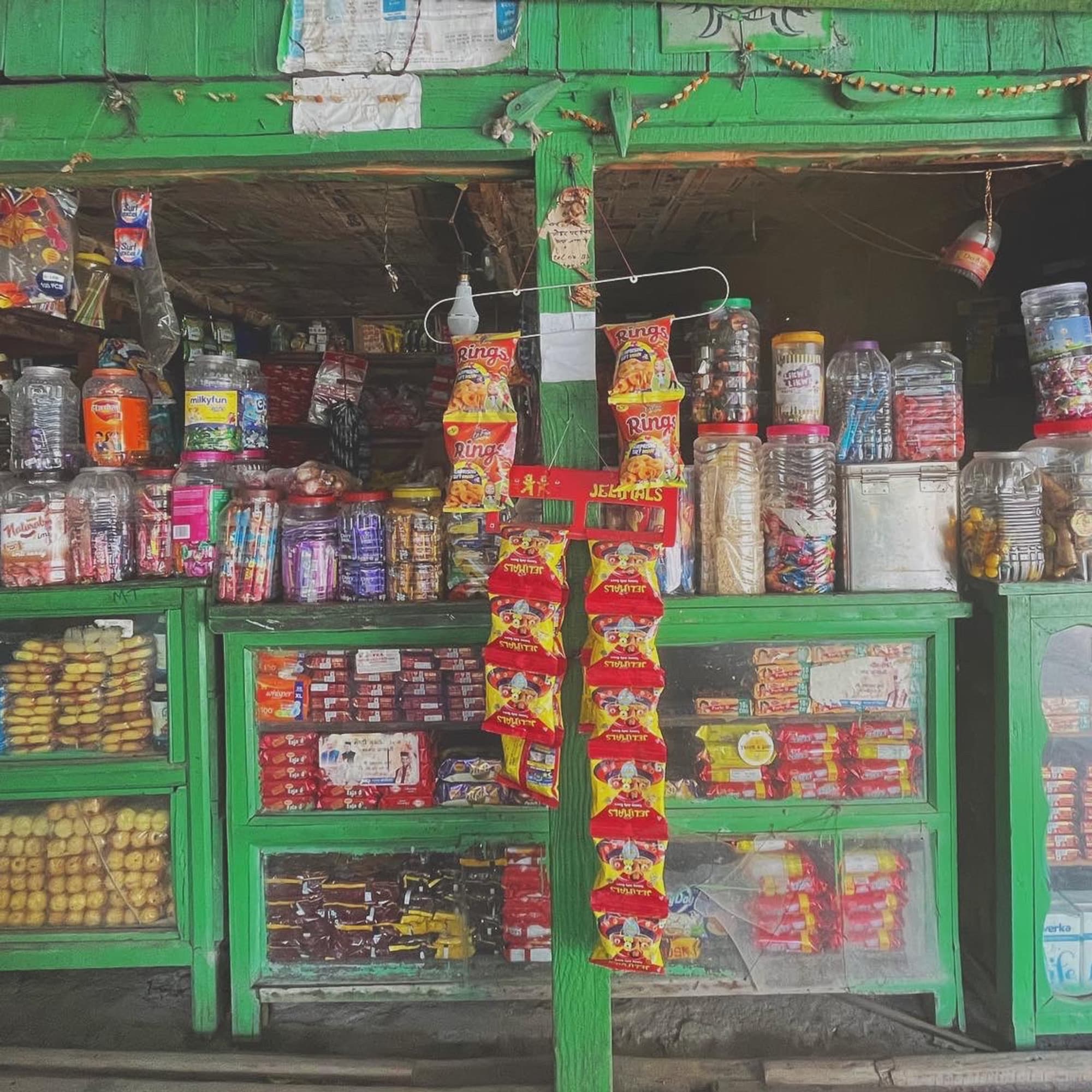A green-painted local shop, shelves stacked with snacks and jars