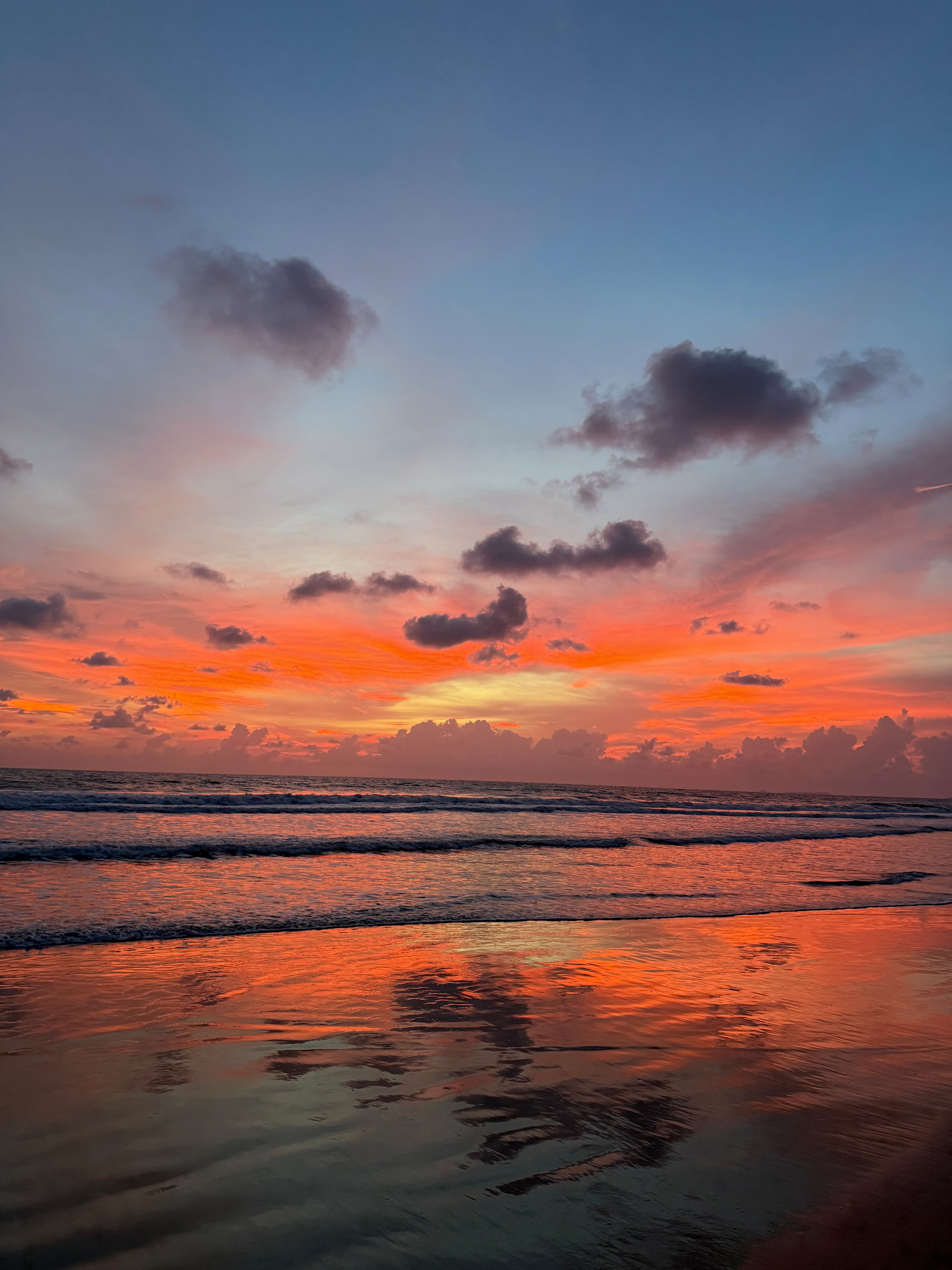 A dramatic orange sunset reflected on the wet sand